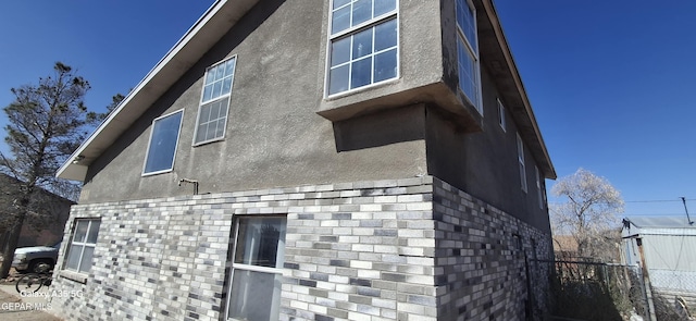 view of property exterior with brick siding, stucco siding, and fence