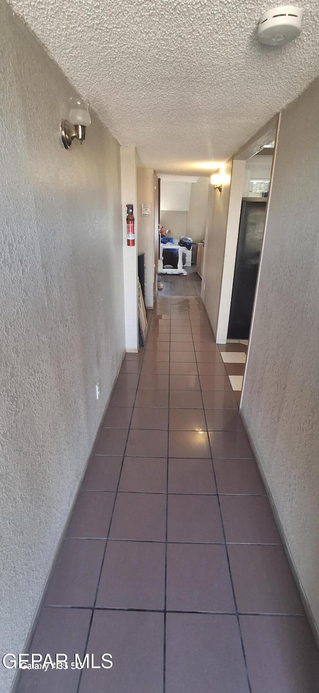 hallway with tile patterned floors, a textured wall, and a textured ceiling