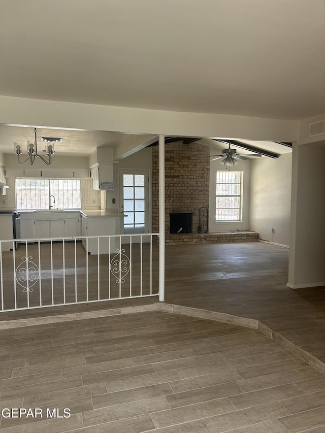2816 Gaston Dr, El Paso, TX 79935 - unfurnished living room featuring a brick fireplace, wood finished floors, a chandelier, ceiling fan, and plenty of natural light