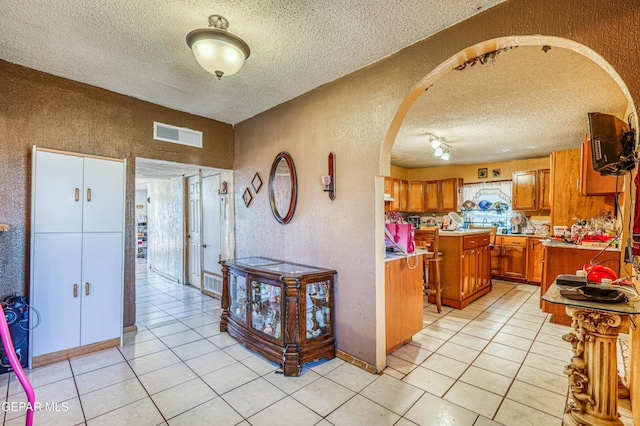 entrance foyer featuring visible vents, arched walkways, light tile patterned flooring, and a textured wall