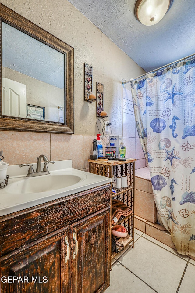 full bath featuring a shower with shower curtain, a textured wall, a textured ceiling, vanity, and tile patterned flooring