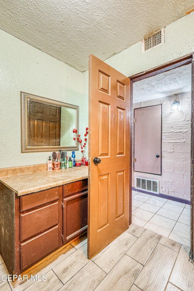 bathroom featuring a textured wall, vanity, visible vents, and a textured ceiling