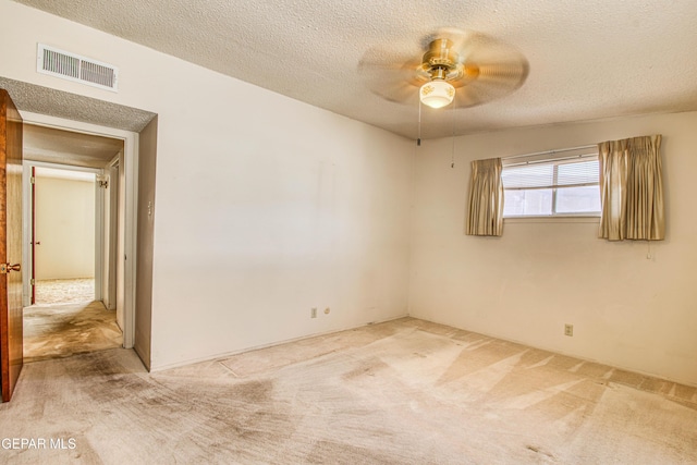 carpeted spare room with visible vents, a textured ceiling, and ceiling fan