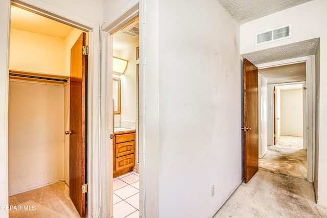 hall with light carpet, visible vents, and a textured ceiling