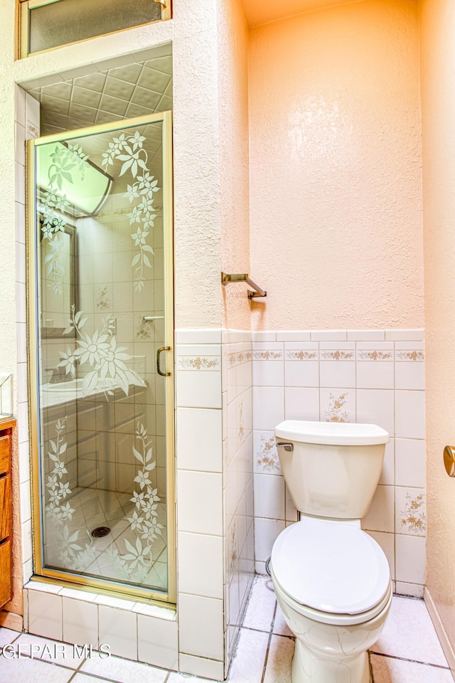 bathroom featuring toilet, a stall shower, tile walls, and tile patterned floors