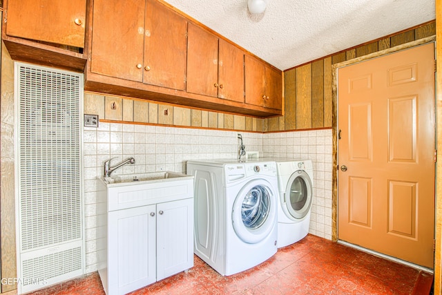 laundry area with a textured ceiling, independent washer and dryer, cabinet space, tile walls, and a sink