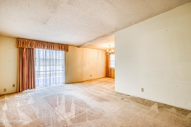 spare room with a textured ceiling, carpet flooring, and an inviting chandelier