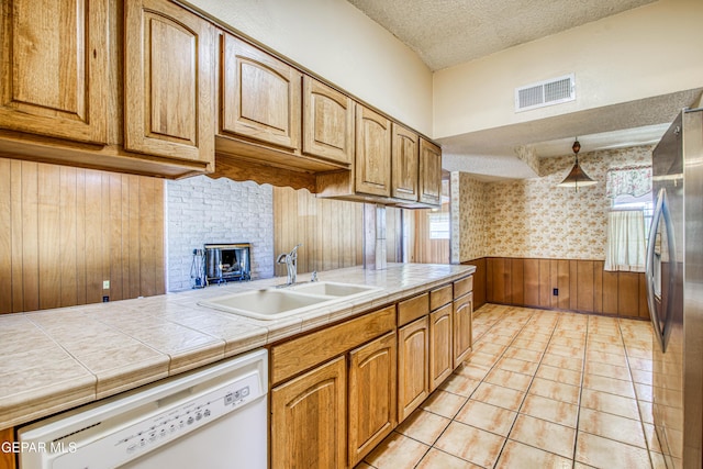 kitchen featuring a textured ceiling, freestanding refrigerator, visible vents, white dishwasher, and a sink