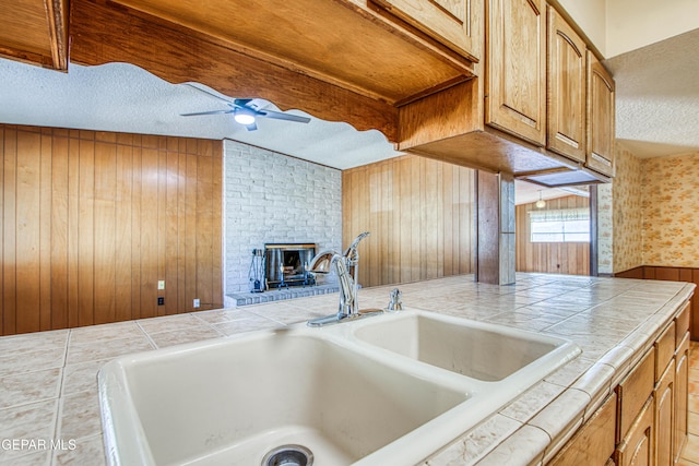 kitchen with wood walls, a textured ceiling, a sink, and tile counters
