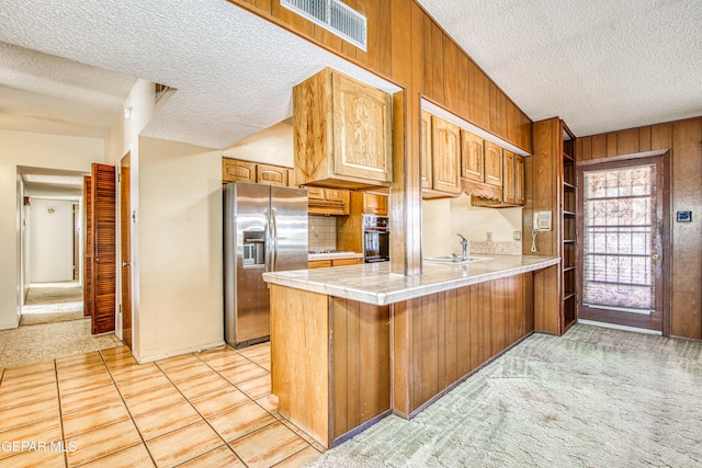 kitchen with stainless steel fridge with ice dispenser, black oven, a peninsula, a textured ceiling, and visible vents
