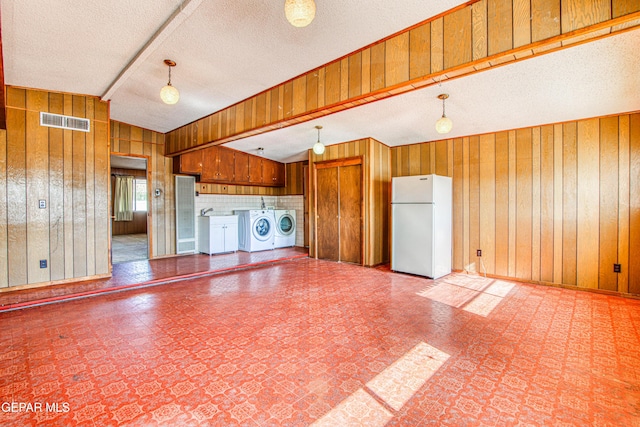 interior space with vaulted ceiling, a textured ceiling, wood walls, visible vents, and independent washer and dryer