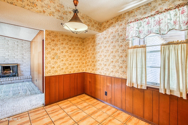 spare room featuring a fireplace, a textured ceiling, light tile patterned flooring, wainscoting, and wallpapered walls
