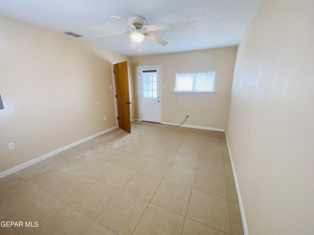 spare room with a textured ceiling, ceiling fan, baseboards, and visible vents