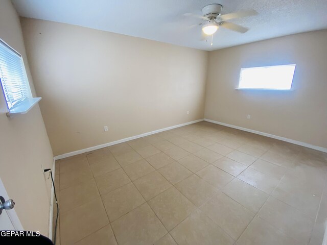 empty room featuring light tile patterned floors, baseboards, a ceiling fan, and a textured ceiling