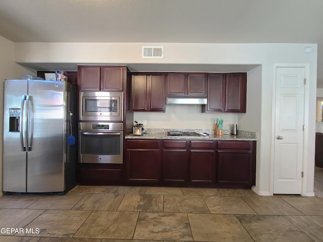 kitchen with light stone counters, stainless steel appliances, reddish brown cabinets, under cabinet range hood, and visible vents