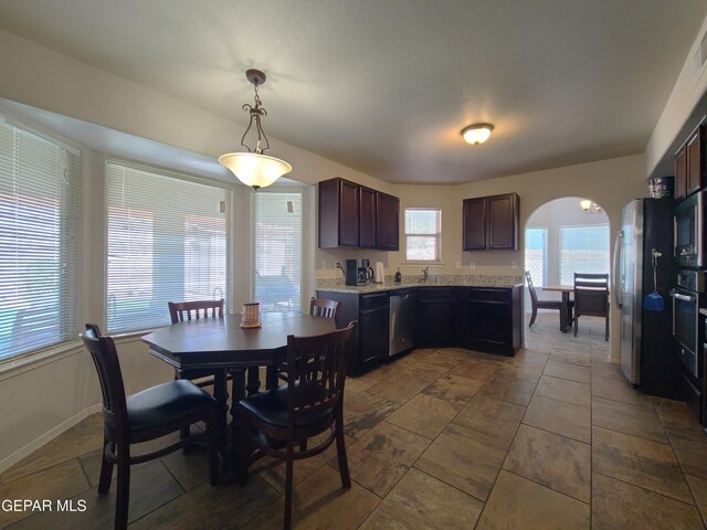 kitchen with dark brown cabinets, baseboards, arched walkways, hanging light fixtures, and stainless steel appliances