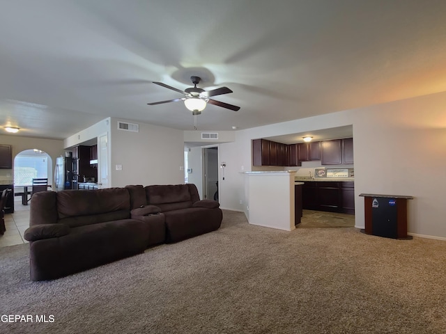 living room featuring visible vents, a ceiling fan, arched walkways, and light colored carpet