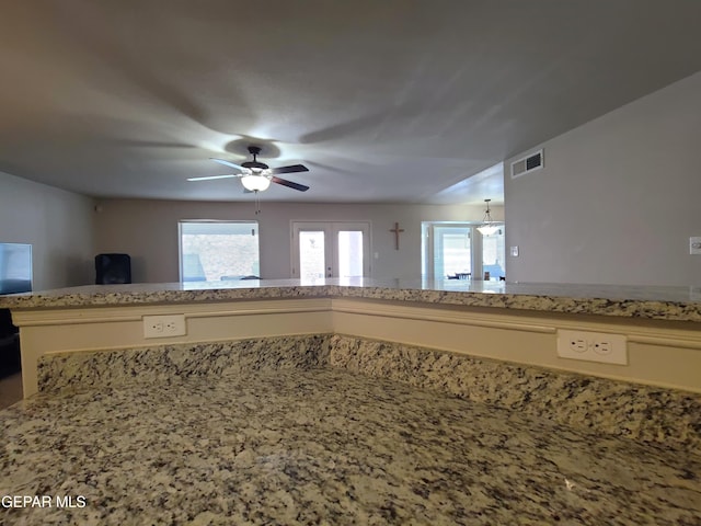 kitchen with light stone counters, ceiling fan, and visible vents
