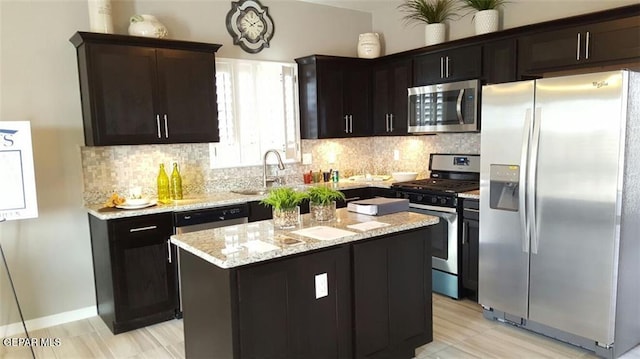 kitchen with appliances with stainless steel finishes, backsplash, light stone counters, and a center island