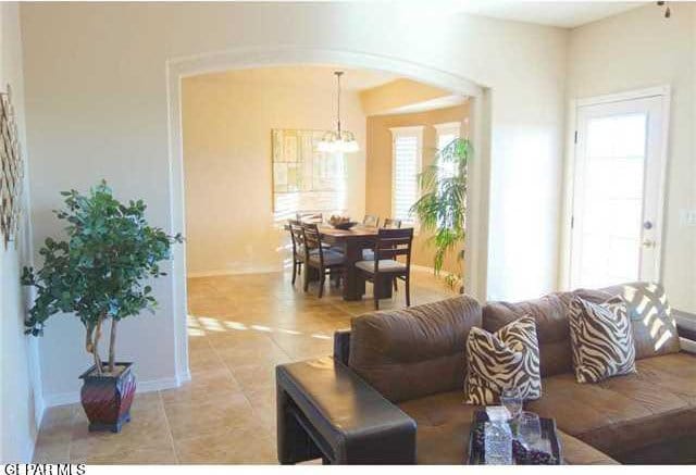 living room featuring arched walkways, a chandelier, light tile patterned flooring, and baseboards