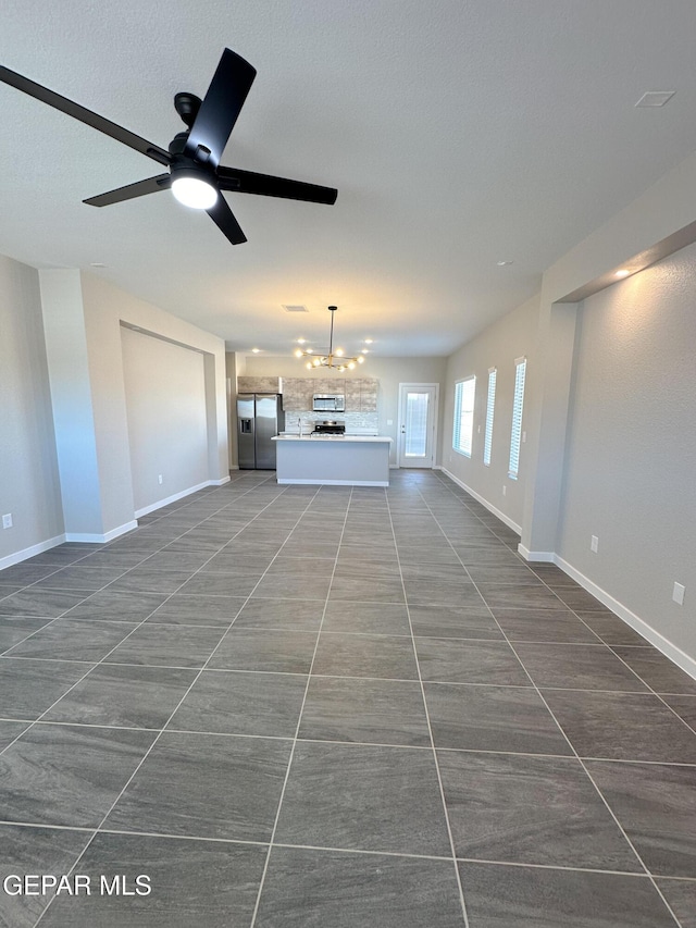 unfurnished living room with ceiling fan with notable chandelier, baseboards, and dark tile patterned flooring