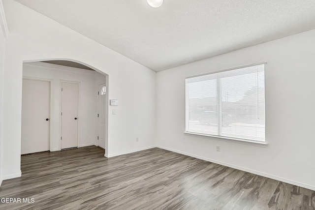 12729 Raul Mendiola Ln, El Paso, TX 79938 - unfurnished room featuring arched walkways, wood finished floors, baseboards, and a textured ceiling