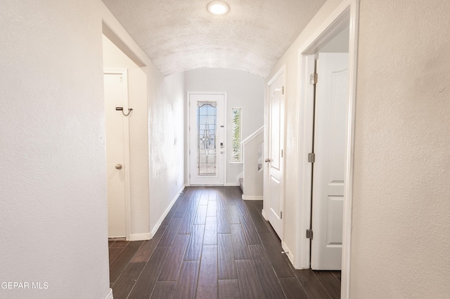 hallway with lofted ceiling, baseboards, dark wood finished floors, and a textured wall