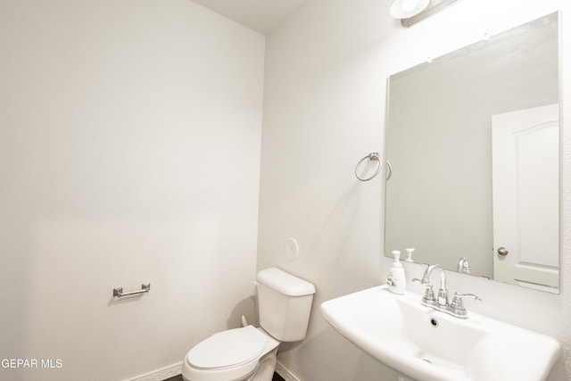 half bath featuring a sink, toilet, and baseboards