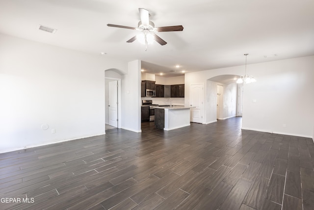 unfurnished living room featuring arched walkways, a ceiling fan, dark wood finished floors, and baseboards