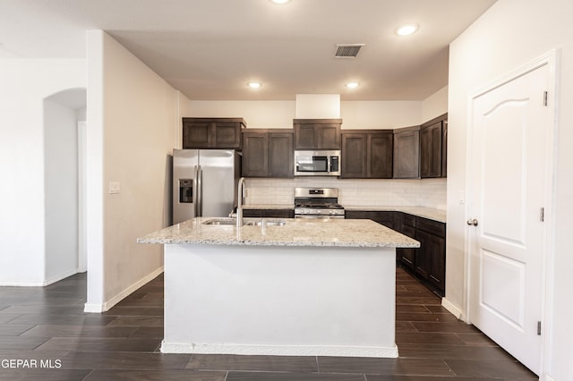 kitchen featuring stainless steel appliances, a sink, dark brown cabinets, tasteful backsplash, and a kitchen island with sink