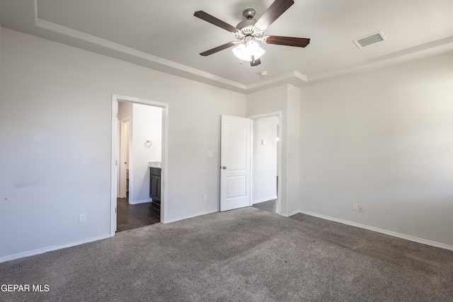 unfurnished bedroom featuring dark carpet, a tray ceiling, baseboards, and ensuite bath