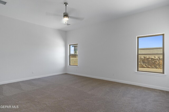 spare room featuring visible vents, a ceiling fan, baseboards, and dark colored carpet
