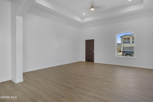 empty room featuring ceiling fan, a tray ceiling, and light wood-style floors