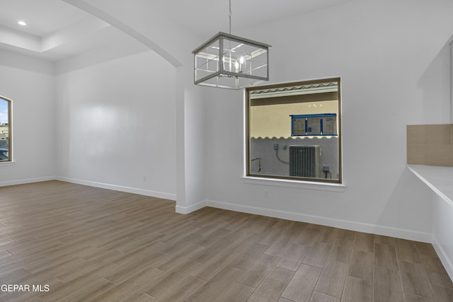 unfurnished dining area featuring a tray ceiling, arched walkways, baseboards, an inviting chandelier, and wood finished floors