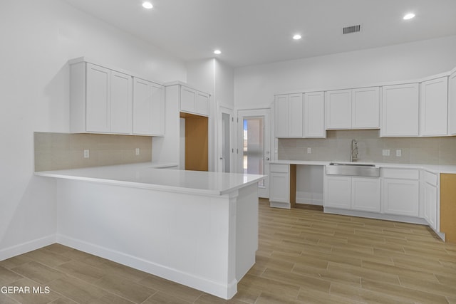 kitchen with visible vents, a sink, light wood-style floors, a peninsula, and tasteful backsplash