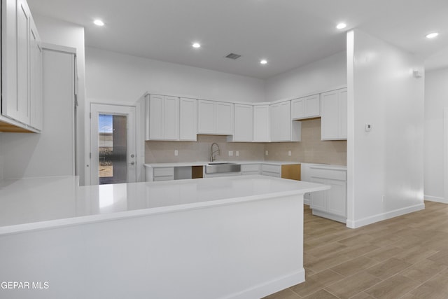 kitchen featuring a sink, decorative backsplash, light wood finished floors, a peninsula, and recessed lighting