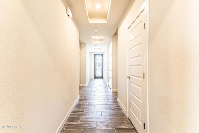 hall featuring a raised ceiling, dark wood finished floors, and baseboards