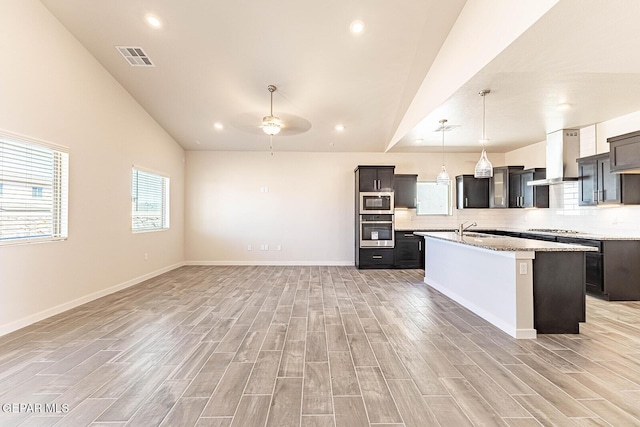 kitchen featuring wall chimney range hood, lofted ceiling, a sink, appliances with stainless steel finishes, and ceiling fan