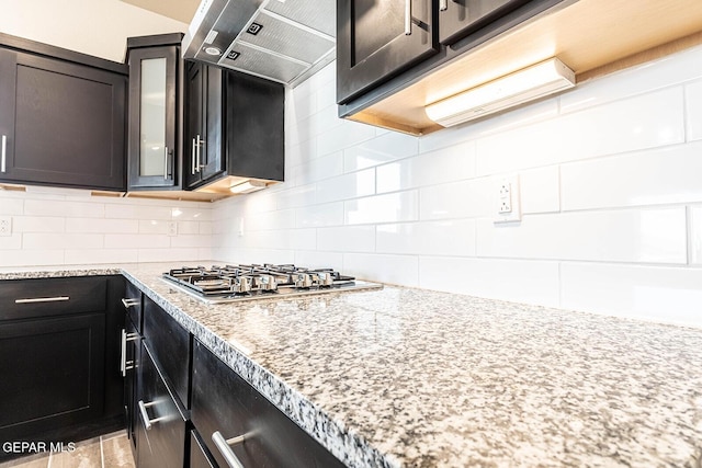 kitchen featuring tasteful backsplash, glass insert cabinets, under cabinet range hood, and stainless steel gas stovetop