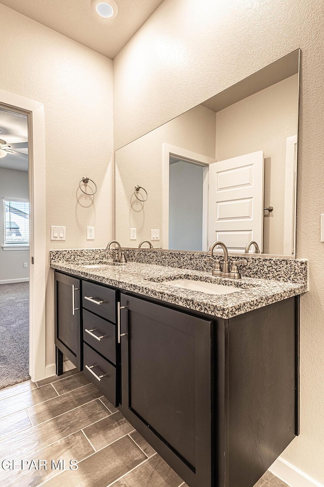 full bath featuring double vanity, wood finished floors, ceiling fan, and a sink