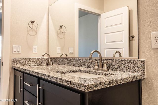 bathroom featuring double vanity, a textured wall, and a sink