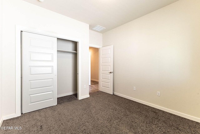 unfurnished bedroom with a closet, visible vents, dark carpet, and baseboards