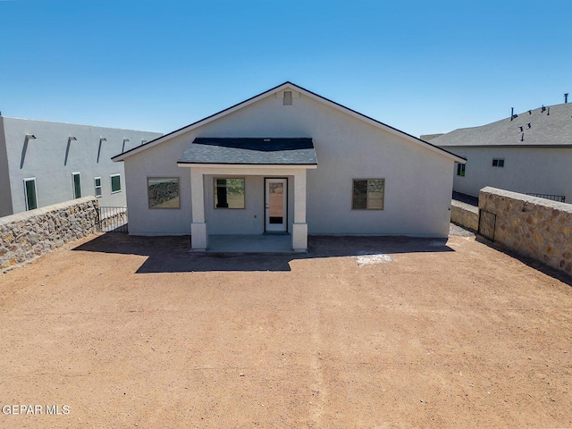 view of front of house with a patio, a fenced backyard, stucco siding, and roof with shingles