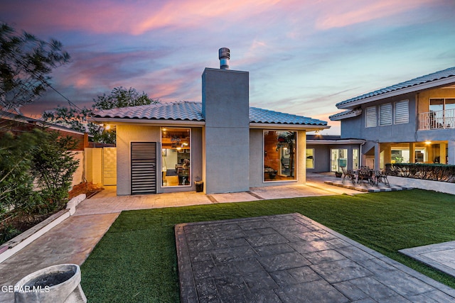 701 La Cruz Dr, El Paso, TX 79902 - back of property at dusk featuring a yard, a patio area, a chimney, a tile roof, and stucco siding