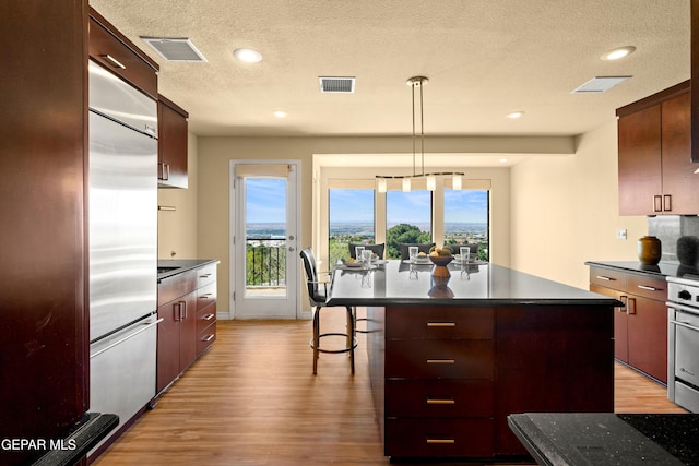 kitchen with light wood-style floors, built in refrigerator, dark countertops, and visible vents