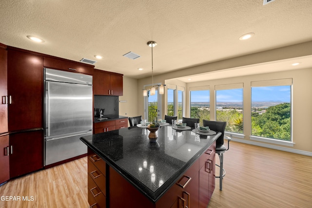 kitchen featuring a kitchen island, light wood-style floors, visible vents, a breakfast bar area, and stainless steel built in fridge