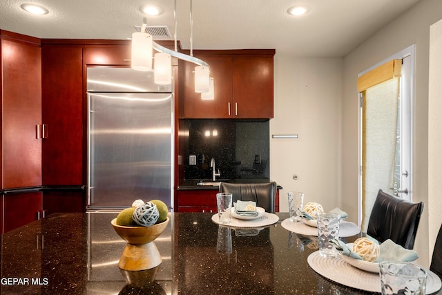 kitchen featuring decorative backsplash, dark stone countertops, stainless steel built in refrigerator, and recessed lighting