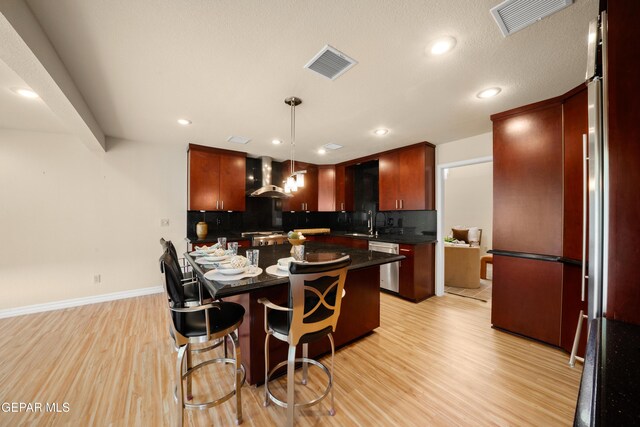 kitchen with stainless steel dishwasher, dark countertops, wall chimney range hood, and visible vents
