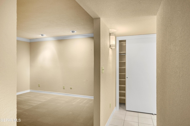 hallway with baseboards, carpet, a textured ceiling, crown molding, and tile patterned flooring
