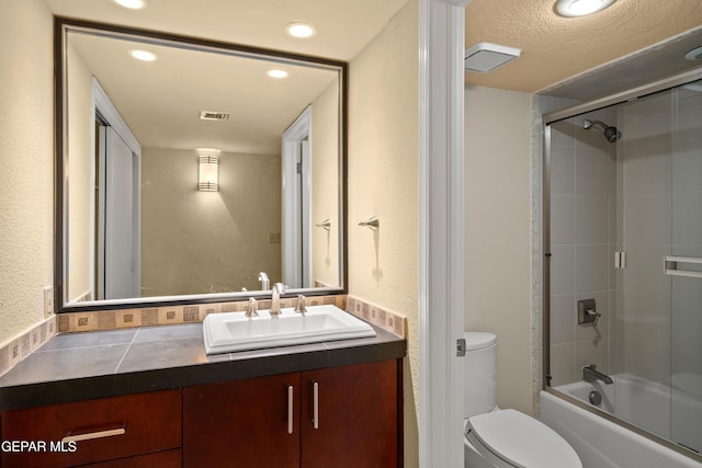 full bath featuring vanity, a textured wall, toilet, visible vents, and bath / shower combo with glass door